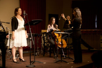 A singer, cellist, and conductor perform onstage