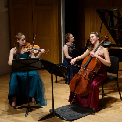 A trio of teenage women playing violin, cello, and piano in a concert