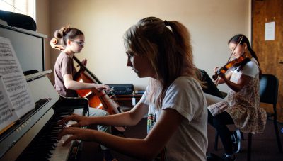 Three young musicians playing piano, cello, and violin in a practice room