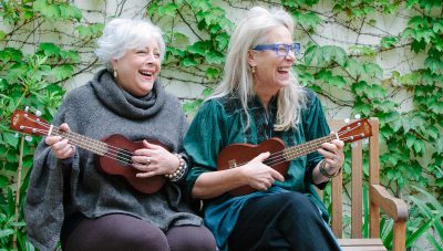 Two adult women playing ukulele and laughing