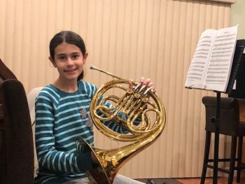 Girl with a french horn in front of a music stand