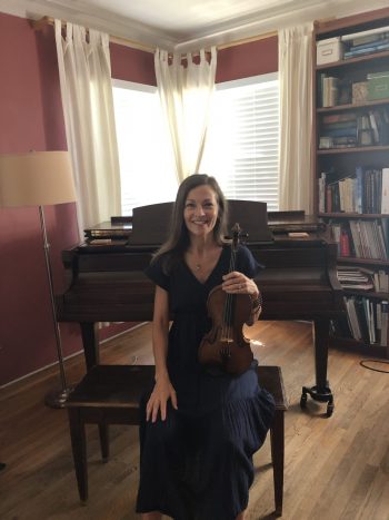 Woman sitting on piano bench with her violin in hand