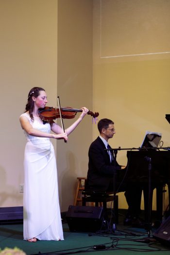 Woman in wedding dress plays viola with man in suit playing piano