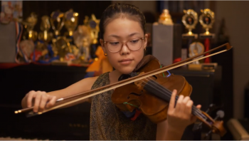 Young girl plays viola in front of trophies