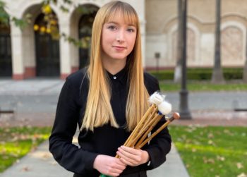 Young Woman with long blonde hair and bangs holding percussion mallets in a courtyard
