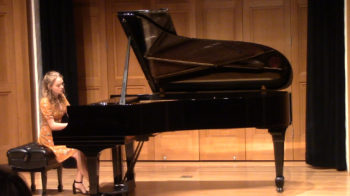 Young blonde woman in a pink dress sitting at the piano