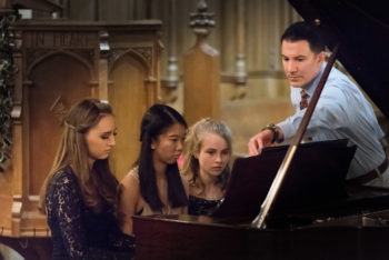 3 young women at the piano being coached by their male teacher