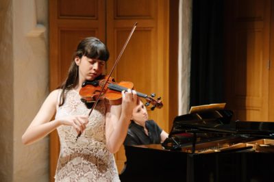 Teen girl plays violin accompanied by pianist.