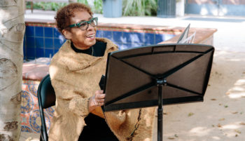 Woman in brown shawl singing outside with a music stand