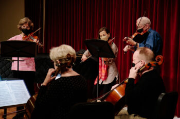 4 adult string musicians on stage masked