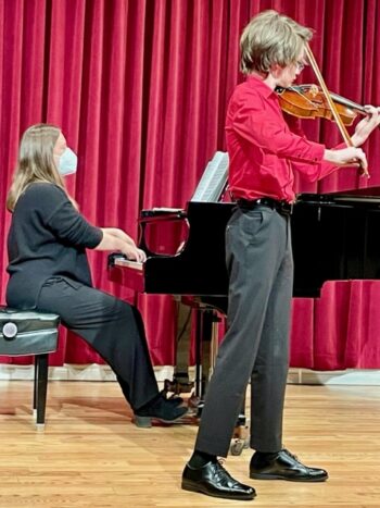 Woman accopanies young man playing violin on piano