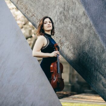 Woman in between two concrete structures holding a violin