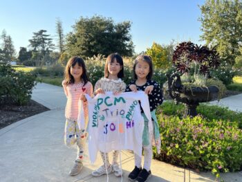 3 young girls holding a sweatshirt they designed for their trio