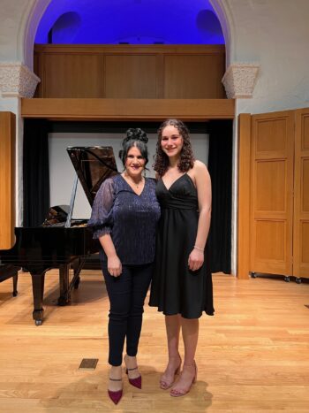 Two women in black pose in a recital hall