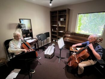 Older man takes a cello lesson. Two men playing cello.