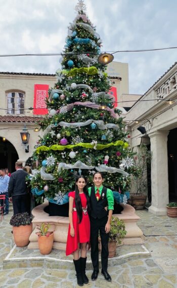 To young adults pose in front of a christmas tree