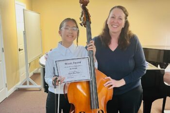 A young bass student poses with her teacher and a certificate