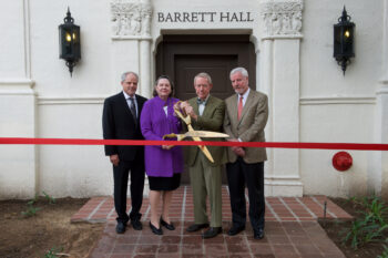 3 men and one woman pose at a ribbon cutting in front of Barrett Hall