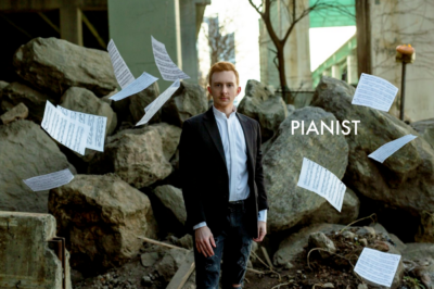 Man stands in front rocks with sheet music raining down around him