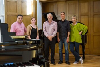 3 men and 2 women pose in front of a piano