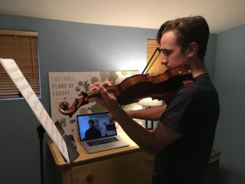 Young man plays violin in his room on a zoom call with his teacher